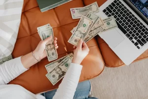 A Woman counts money in front of her laptop.